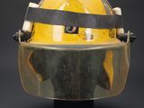 yellow fireman ' s helmet on a black stand against a black background