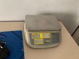 une photo montrant une balance numérique posée sur une table, avec un appareil photo à côté