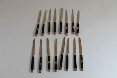 six knives are lined up on a white surface with a black handle