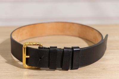 ceinture en cuir noir avec boucle dorée posée sur une surface en bois