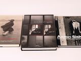 trois livres posés sur une table blanche, accompagnés d'une photo en noir et blanc les représentant