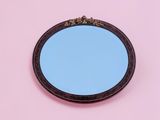 un gros plan sur un miroir posé sur une surface rose, avec un ciel bleu en arrière-plan