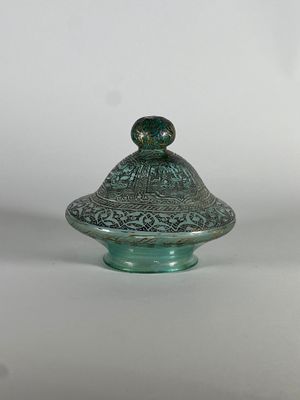 une image représentant un récipient en verre vert muni d'un couvercle, posé sur une surface blanche
