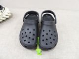 two pairs of black crocs are on the floor next to a pair of white shoes