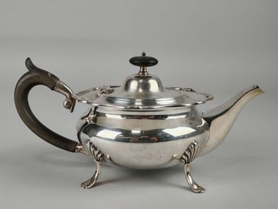 a silver teapot with a handle on a stand on a grey background
