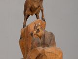 a wooden sculpture of a goat on top of a rock