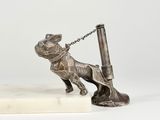 statue en argent représentant un chien tenant un stylo, posée sur un socle en marbre