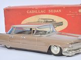 une petite voiture devant une boîte contenant des berlines Cadillac, posée sur une surface blanche