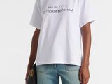Une femme vêtue d'un t-shirt blanc et d'un jean se tient debout devant un fond blanc.