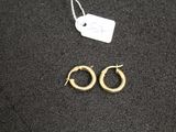 une paire de boucles d'oreilles créoles en or posées sur une surface noire, avec une étiquette de prix