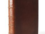 an old book with a brown cover sitting on a white surface