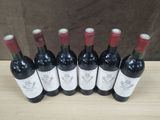 six bottles of red wine lined up on a wooden table