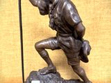 statue en bronze représentant un homme tenant un bâton, assis sur un rocher