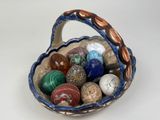 un panier rempli de pierres de différentes couleurs posé sur une surface blanche
