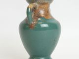 a green vase with a brown handle sitting on a white surface