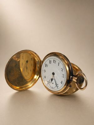 une montre de poche en or posée sur une table, sur fond blanc
