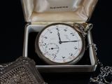 a silver pocket watch sitting in a box with a chain around it