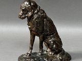 statue en bronze représentant un chien assis sur un rocher, posée sur un socle gris