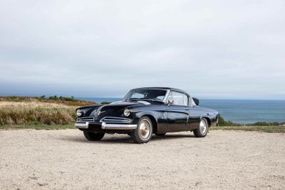 an old black car parked on a gravel road near the ocean