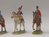 four figurines of men in uniforms riding horses on a white surface