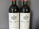 two bottles of red wine sitting on top of a wooden table