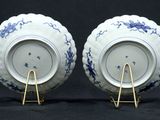 two blue and white plates with gold stands on a black background