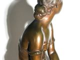 bronze statue of a woman sitting on a rock with her hands on her knees