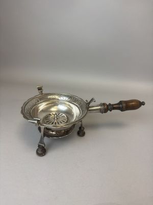 une assiette ancienne en argent avec un manche en bois, posée sur une surface blanche