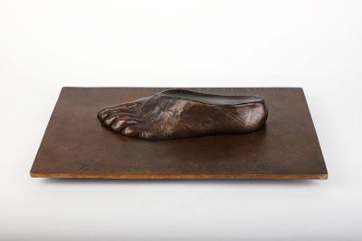 sculpture représentant un pied posé sur une planche en bois, sur fond blanc
