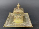 an antique brass inkwell on a tray on a black background