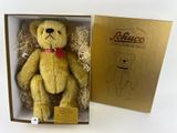 un ours en peluche jaune dans une boîte, avec un nœud papillon rouge