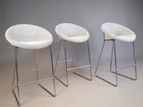 three white wicker bar stools with chrome legs against a gray wall