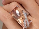 une image représentant la main d'une femme tenant une bague sertie d'un diamant orange