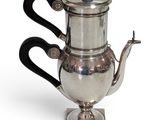 a silver tea pot with a black handle on a stand
