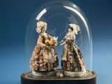 two figurines that are under a glass dome on a table