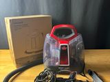 un aspirateur rouge et noir posé sur une table en bois, à côté d'une boîte