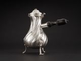 une cafetière ancienne en argent avec une anse, sur fond noir
