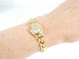 wrist of a woman wearing a gold watch with a chain around her wrist