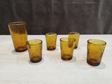 six yellow glass tumblers sitting on top of a wooden table