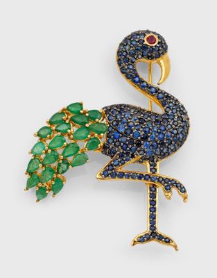 un gros plan sur une broche en forme d'oiseau ornée de pierres bleues et vertes