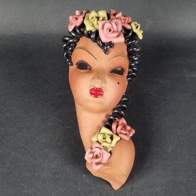 une tête de femme en argile, avec des fleurs dans les cheveux