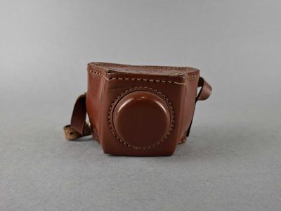 brown leather camera case with a small lens on a gray surface