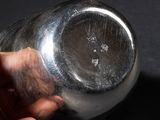 a hand holding a silver vase on a black surface