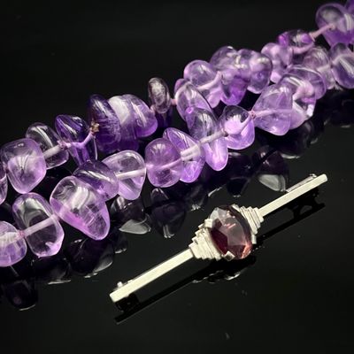 des perles d'améthorate violettes et une broche en argent sur un fond noir