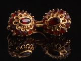 une paire de boucles d'oreilles en or ornées de grenats sur un fond noir