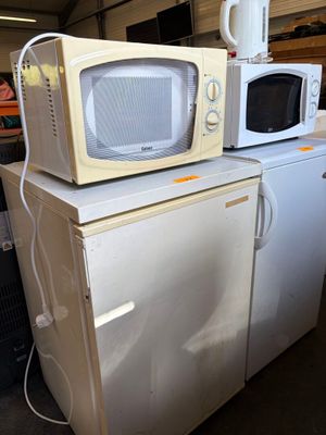 two microwaves sitting on top of a refrigerator in a garage