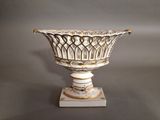 un vase blanc et doré posé sur un socle, sur fond gris