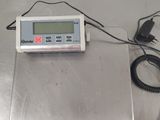une balance numérique posée sur une surface métallique, avec un cordon