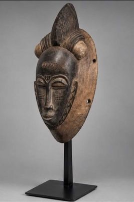 un masque en bois muni de cornes, posé sur un socle, sur fond gris