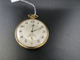 une montre de poche en or posée sur une surface noire, avec une étiquette blanche